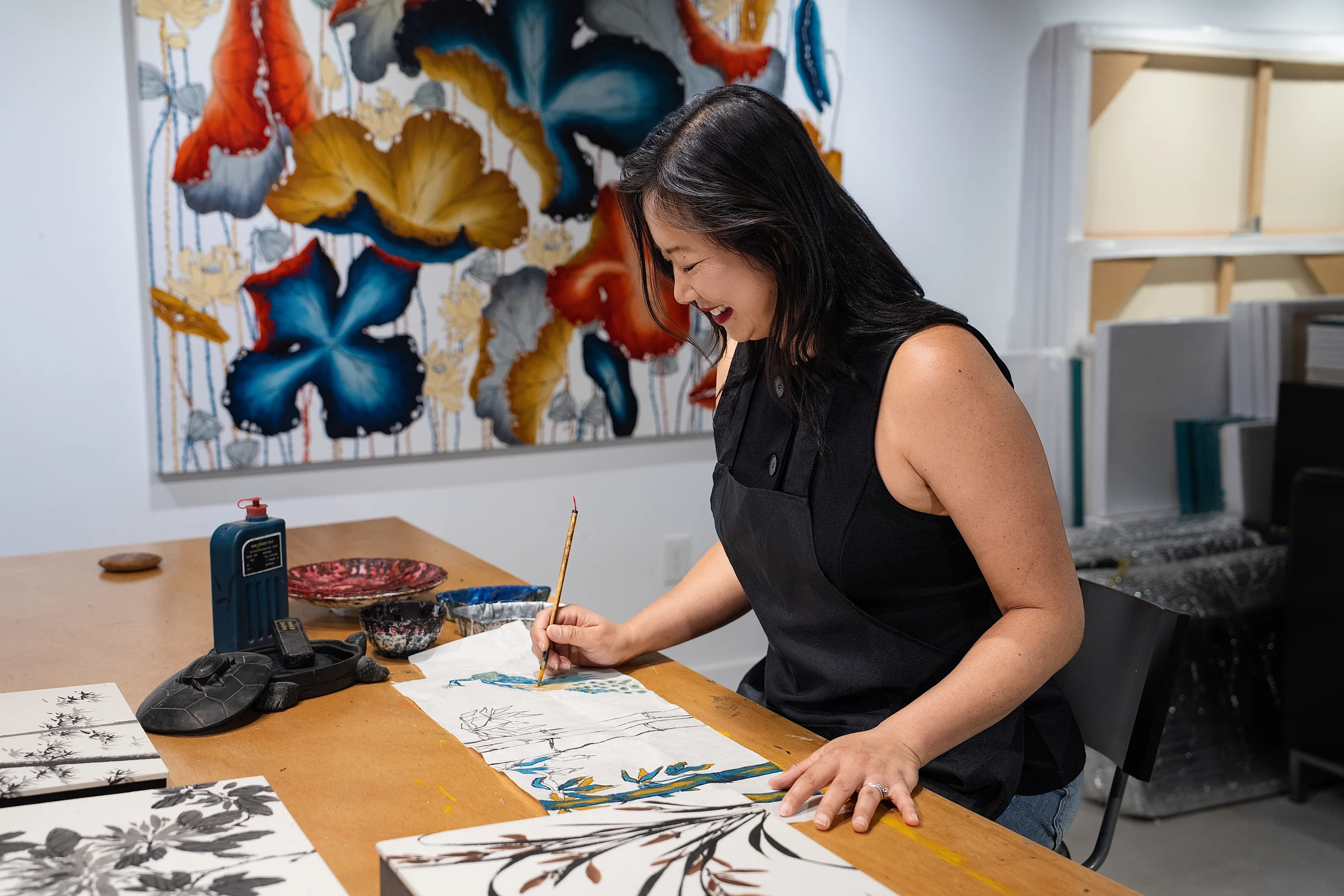 Nha Vuu painting at her studio table, surrounded by original artwork and brushes